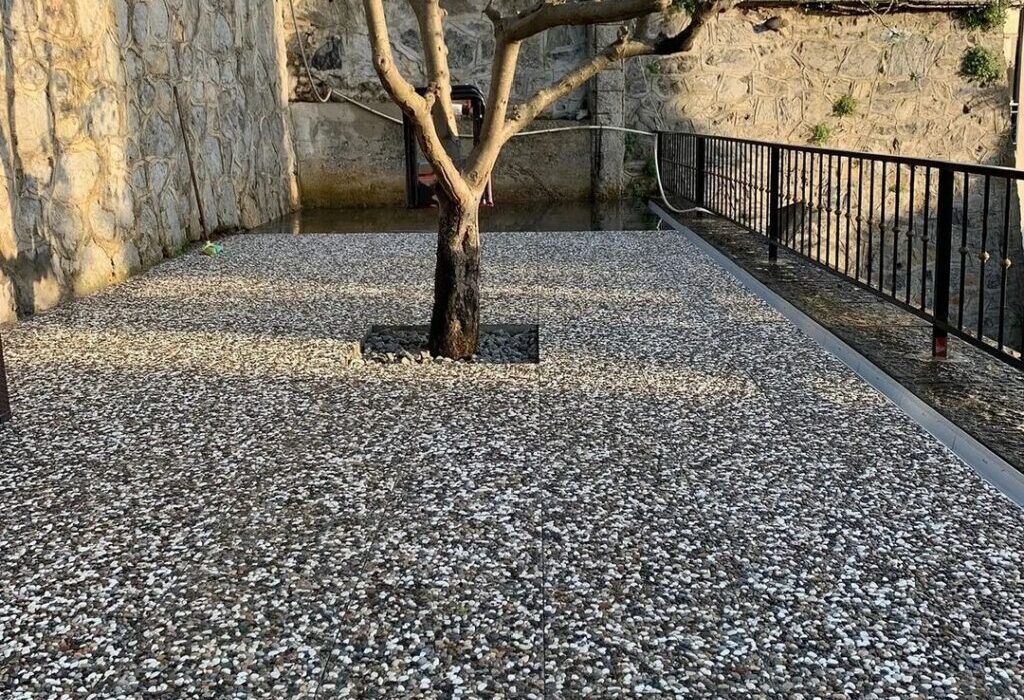 Wash beton karolarla kaplanmış, ortasında ağaç bulunan modern peyzaj zemin uygulaması. Gri ve beyaz doğal çakıl görünümlü karolar.