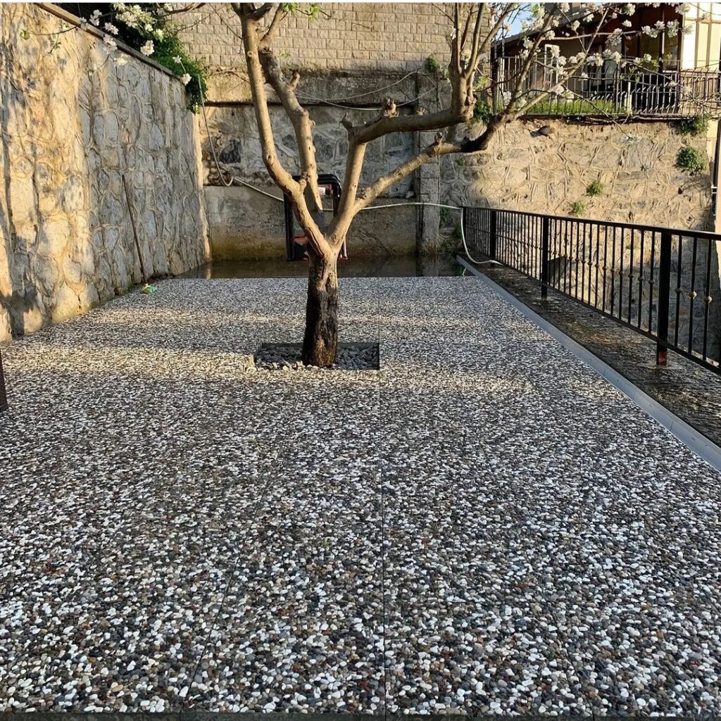 Wash beton karolarla kaplanmış, ortasında ağaç bulunan modern peyzaj zemin uygulaması. Gri ve beyaz doğal çakıl görünümlü karolar.