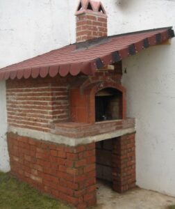 Kırmızı tuğla ile örülmüş, kemerli fırın ağzı ve kiremit desenli shingle çatısı olan geleneksel bahçe fırını. Alt kısımda odunluk bölmesi.