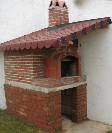 Kırmızı tuğla ile örülmüş, kemerli fırın ağzı ve kiremit desenli shingle çatısı olan geleneksel bahçe fırını. Alt kısımda odunluk bölmesi.