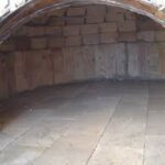 Kırmızı tuğladan kaidesi ve odunluğu örülmüş, kırmızı sıvalı kubbesi ve uzun tuğla bacası olan modern bahçe fırını.