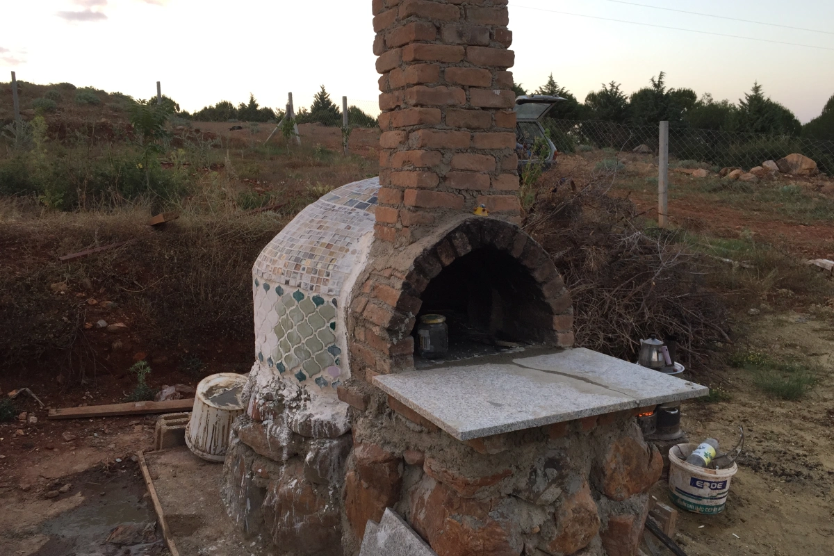 Killi toprak üzerinde, tuğla bacalı ve kubbesi mozaik kaplama detayıyla tamamlanmaya yakın hobi bahçesi fırını.