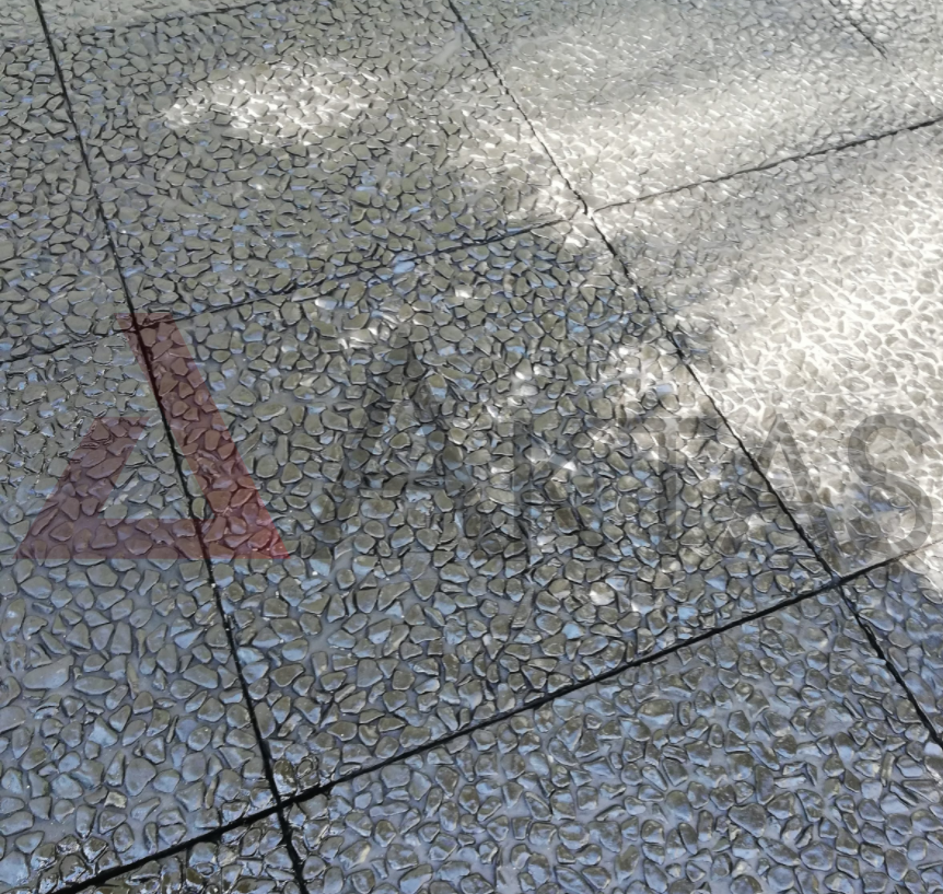 Siyah veya koyu gri çakılların baskın olduğu, güneş ışığı yansımasıyla parlak görünen wash beton karoların zemin uygulaması.