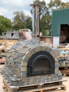 Doğal kayrak taşlarıyla kaplanmış, siyah metal kapaklı ve paslanmaz çelik bacalı hazır taş fırın (pizza fırını).