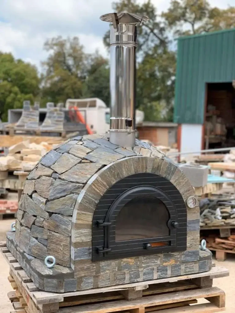 Doğal kayrak taşlarıyla kaplanmış, siyah metal kapaklı ve paslanmaz çelik bacalı hazır taş fırın (pizza fırını).