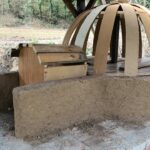 Ahşap çatılı bir alanda, beyaz sıva ve kırmızı tuğla ile inşa edilmiş fırın, barbekü, ocak ve odunluk bölümleri olan entegre bir dış mekan mutfağı.