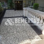 Siyah bordür ile çerçevelenmiş, bej ve gri çakıllı 40x40 wash beton karo ile kaplanmış bina giriş rampası ve avlusu.