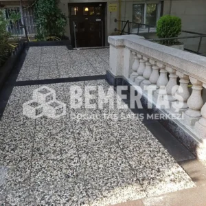 Siyah bordür ile çerçevelenmiş, bej ve gri çakıllı 40x40 wash beton karo ile kaplanmış bina giriş rampası ve avlusu.