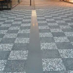 Beyaz ve kahverengi çakıllı wash beton karolarla döşenmiş, ortasında ağaç olan geniş dış mekan zemin uygulaması.