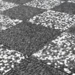 Siyah ve beyaz çakıllı wash beton karolarla yapılmış dama desenli dış mekan zemin uygulaması ve farklı renk çakılların sergilendiği numune panosu.