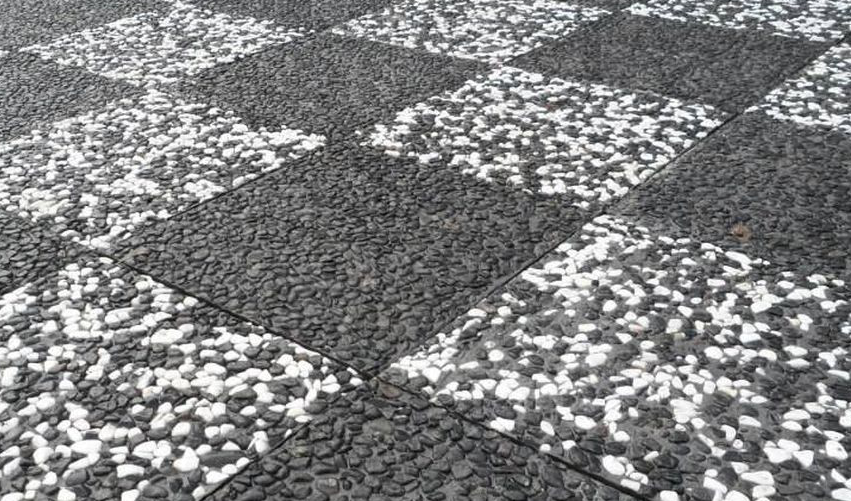 Siyah ve beyaz çakıllı wash beton karolarla yapılmış dama desenli dış mekan zemin uygulaması ve farklı renk çakılların sergilendiği numune panosu.