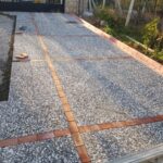 Kırmızı tuğla bordürlerle çapraz kesilmiş ve döşenmiş doğal çakıl agregalı wash beton karodan yapılmış araç giriş yolu.