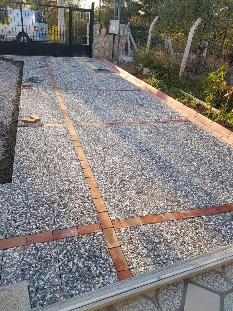 Kırmızı tuğla bordürlerle çapraz kesilmiş ve döşenmiş doğal çakıl agregalı wash beton karodan yapılmış araç giriş yolu.