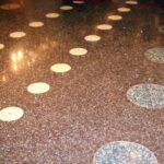 Koyu kahverengi/siyah zeminde beyaz, dairesel mozaik desenleri bulunan, yüksek parlaklıkta cilalanmış terrazzo (dökme mozaik) zemin.