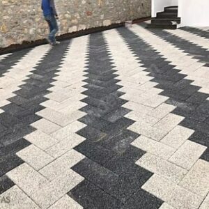 Siyah ve beyaz renklerde, balıksırtı (zikzak) deseninde döşenmiş dikdörtgen prizma parke taşı zemin kaplaması.