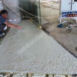 Usta, ahşap kalıbın içindeki kalın agregalı çimento bazlı terrazzo harcını zemin üzerine yayıyor. Dökme mozaik şap uygulama anı.