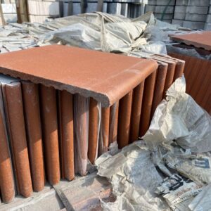 Şantiye alanında üst üste dizilmiş kırmızı renkli, yuvarlak burunlu cotto pişmiş toprak merdiven basamak karoları.