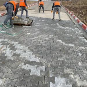 Gri beton kilit taşlarını dış mekânda hazırlanan zemine döşeyen uygulama ekibi