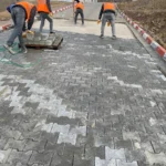 Gri kilitli beton parke taşlarını hazırlanan zemine döşeyen uygulama ekibi
